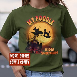 May include: A green t-shirt with the text "My Poodle Rides Shotgun" in white and orange. The design features a witch flying on a broomstick with a poodle in front of a full moon and a haunted house.