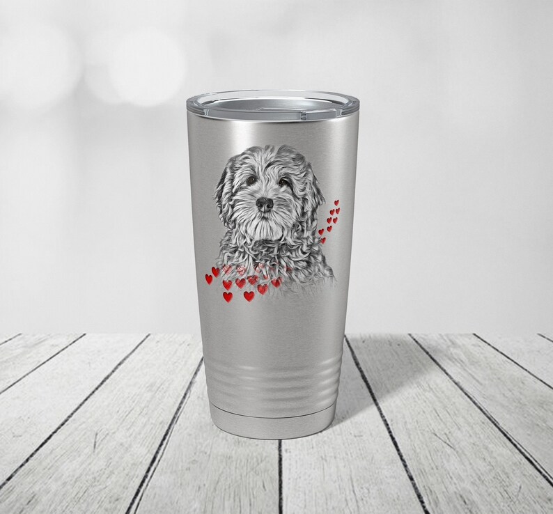 May include: A silver insulated travel mug with a grayscale illustration of a fluffy dog and red heart accents. The dog portrait is surrounded by small red hearts. The travel mug has a silver lid, perfect for hot or cold beverages.