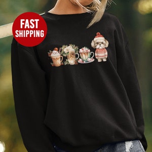 May include: Black sweatshirt with a festive design featuring a dog wearing a Santa hat and surrounded by mugs of hot chocolate with marshmallows and whipped cream.