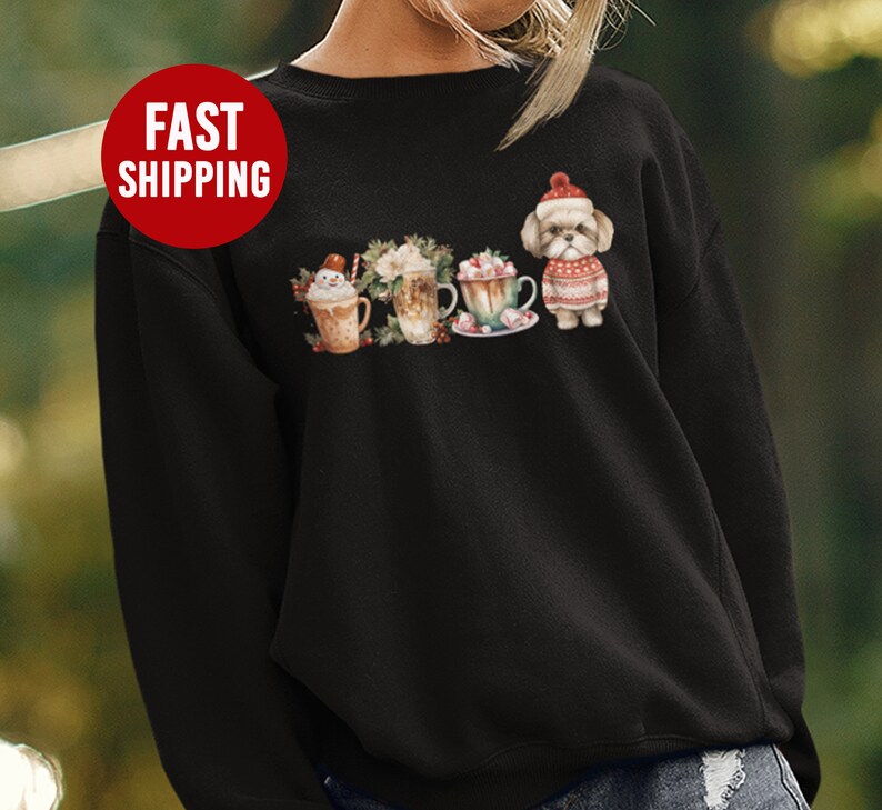May include: Black sweatshirt with a festive design featuring a dog wearing a Santa hat and surrounded by mugs of hot chocolate with marshmallows and whipped cream.