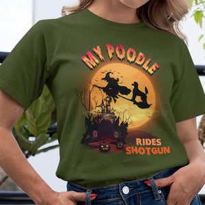May include: A green t-shirt with a graphic of a poodle riding a broomstick with a witch in front of a full moon. The text "My Poodle Rides Shotgun" is printed on the shirt.