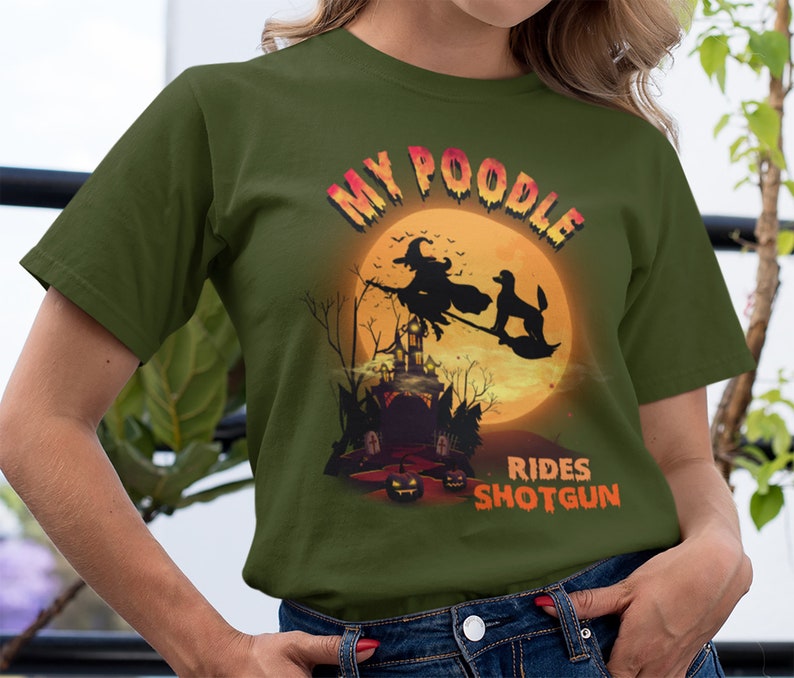 May include: A green t-shirt with a graphic of a poodle riding a broomstick with a witch in front of a full moon. The text "My Poodle Rides Shotgun" is printed on the shirt.
