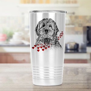 May include: A white stainless steel travel mug with a black and white dog illustration and red heart details. The mug has a silver lid and a ridged design near the base. The mug is suitable for hot or cold drinks.