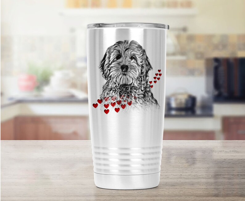 May include: A white stainless steel travel mug with a black and white dog illustration and red heart details. The mug has a silver lid and a ridged design near the base. The mug is suitable for hot or cold drinks.