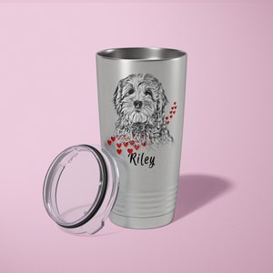 May include: A silver insulated travel mug featuring a black and white dog illustration, with red hearts and the name "Riley". The lid is detached. The mug is designed to keep drinks hot or cold.
