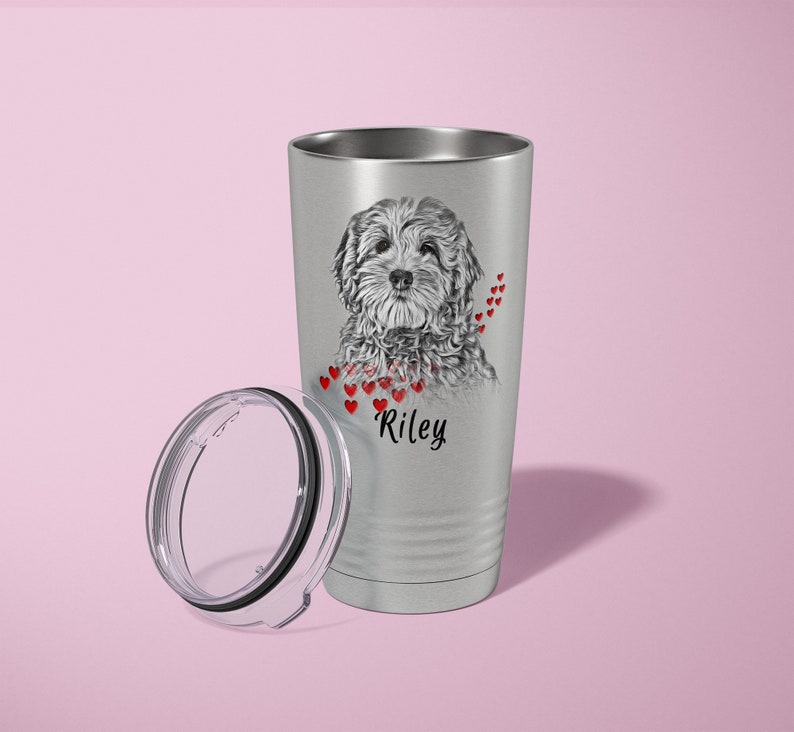 May include: A silver insulated travel mug featuring a black and white dog illustration, with red hearts and the name "Riley". The lid is detached. The mug is designed to keep drinks hot or cold.