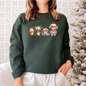 May include: A dark green sweatshirt with a festive design featuring a dog wearing a Santa hat and four mugs of hot chocolate with whipped cream and candy canes.