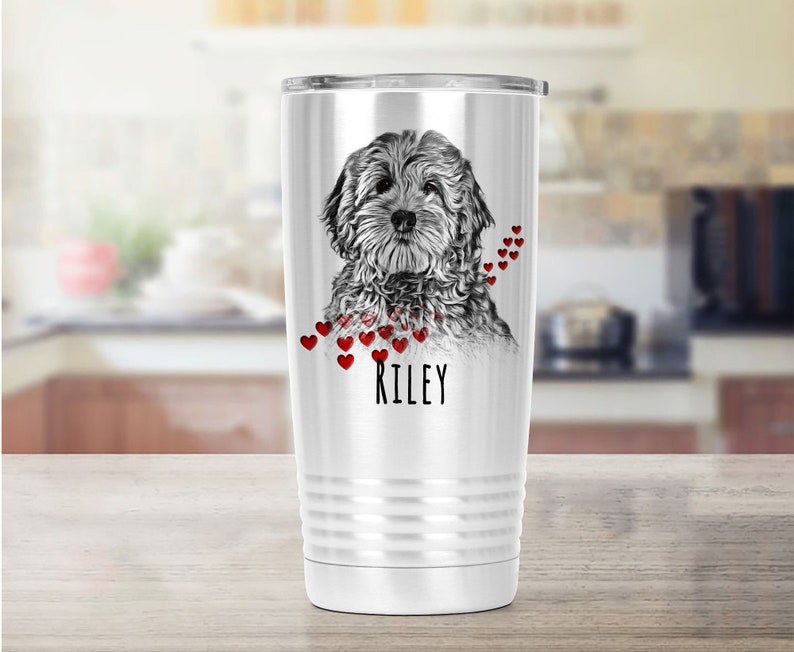 May include: A white stainless steel travel mug with a black and white dog portrait and red heart details. The name "RILEY" is printed in black. The mug has a silver lid and a ridged design. Ideal for hot or cold drinks.
