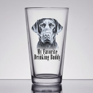 May include: A clear glass pint glass with a black Labrador Retriever dog illustration and the text "My Favorite Drinking Buddy".