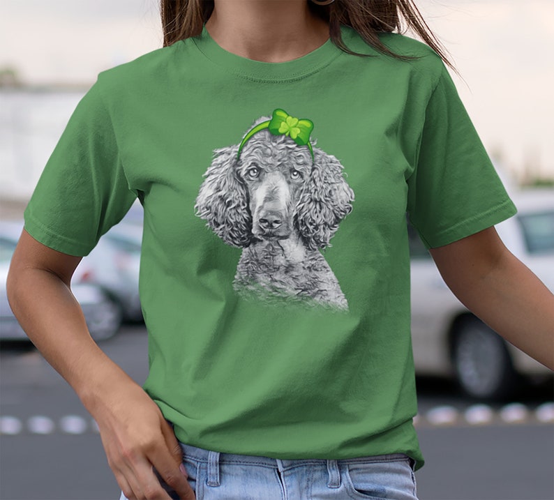 Pu&ograve; includere: Una maglietta verde con un'illustrazione in bianco e nero di un barboncino che indossa un cerchietto verde a forma di trifoglio.