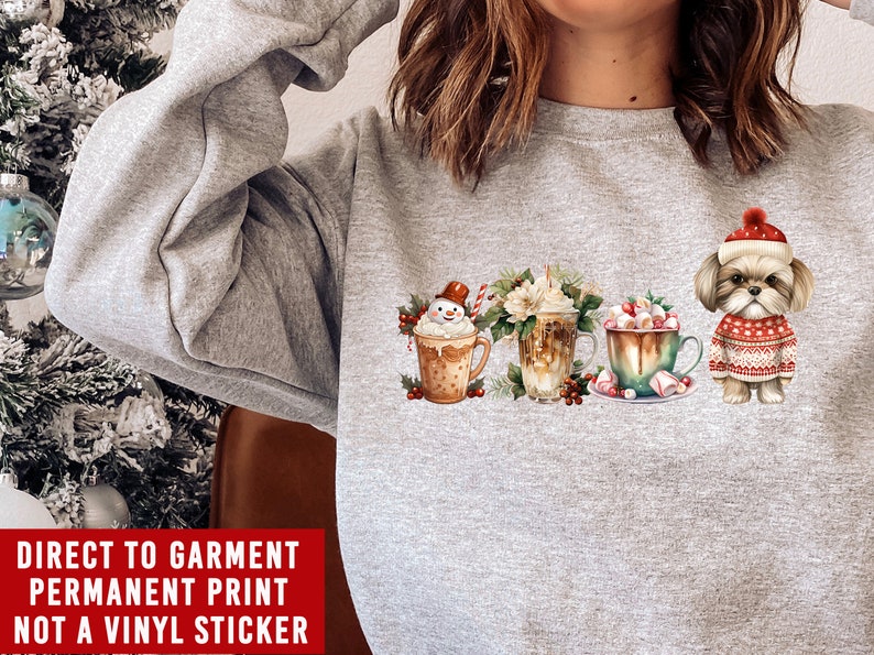 May include: A gray sweatshirt with a Christmas-themed design featuring a snowman, a cup of coffee, a cup of hot chocolate, and a dog wearing a Santa hat. The text "DIRECT TO GARMENT PERMANENT PRINT NOT A VINYL STICKER" is printed on the bottom of the sweatshirt.