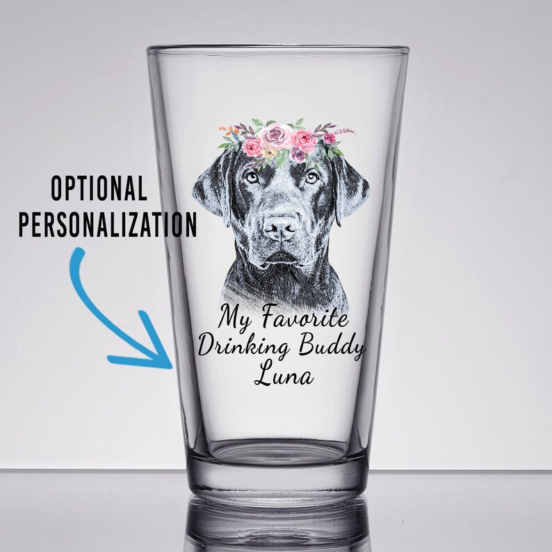 May include: A clear glass pint glass with a black Labrador Retriever wearing a floral crown. The text "My Favorite Drinking Buddy Luna" is printed on the glass.