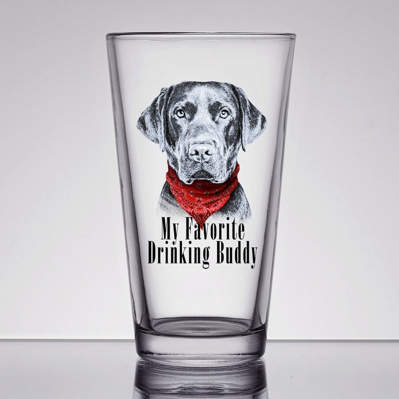 May include: A black and white illustration of a black labrador wearing a red bandana on a clear glass pint glass. The text "My Favorite Drinking Buddy" is printed on the glass.