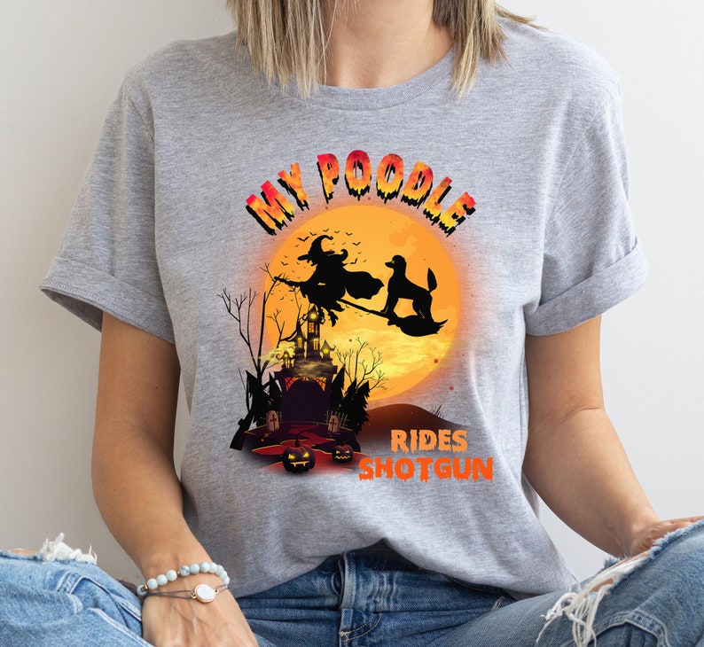May include: Gray t-shirt with a graphic of a poodle riding a broomstick with a witch in front of a full moon and a haunted house. The text reads "My Poodle Rides Shotgun".