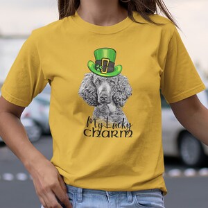 Pu&ograve; includere: Una maglietta gialla con un barboncino grigio che indossa un cappello verde da folletto. Il testo "My Lucky Charm" &egrave; stampato sulla maglietta.