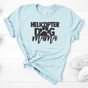 May include: A light blue t-shirt with the text "Helicopter Dog Mama" in black lettering. A paw print is incorporated into the text.