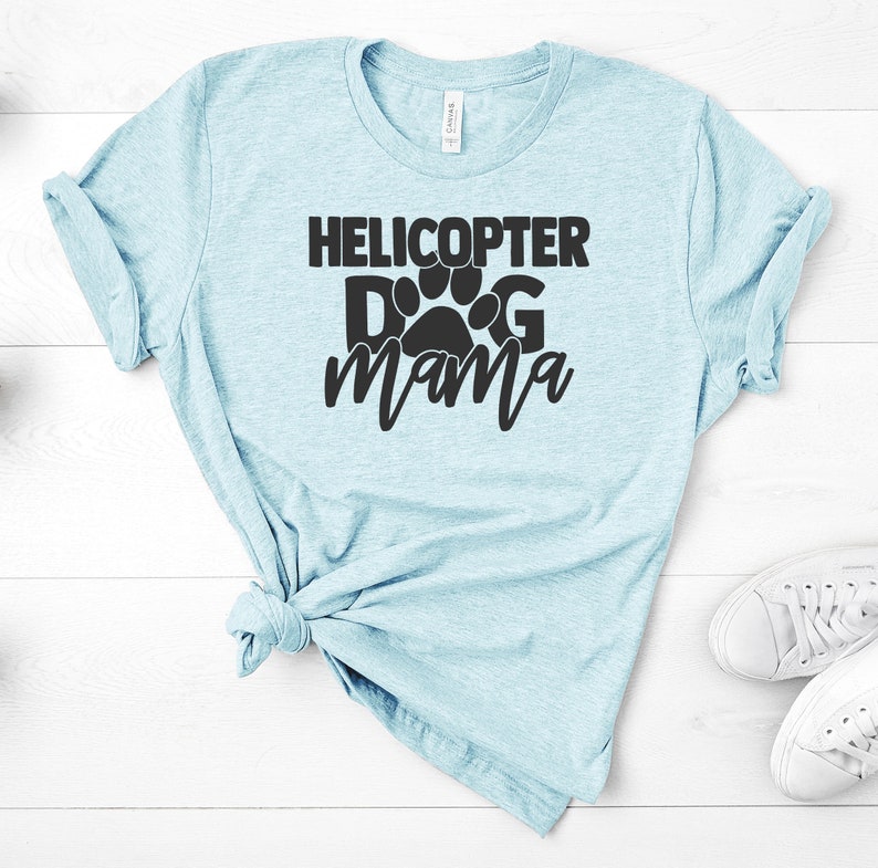 May include: A light blue t-shirt with the text "Helicopter Dog Mama" in black lettering. A paw print is incorporated into the text.