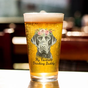 May include: A clear glass beer mug with a black Labrador Retriever wearing a floral crown. The mug has the text "My Favorite Drinking Buddy" printed on it.