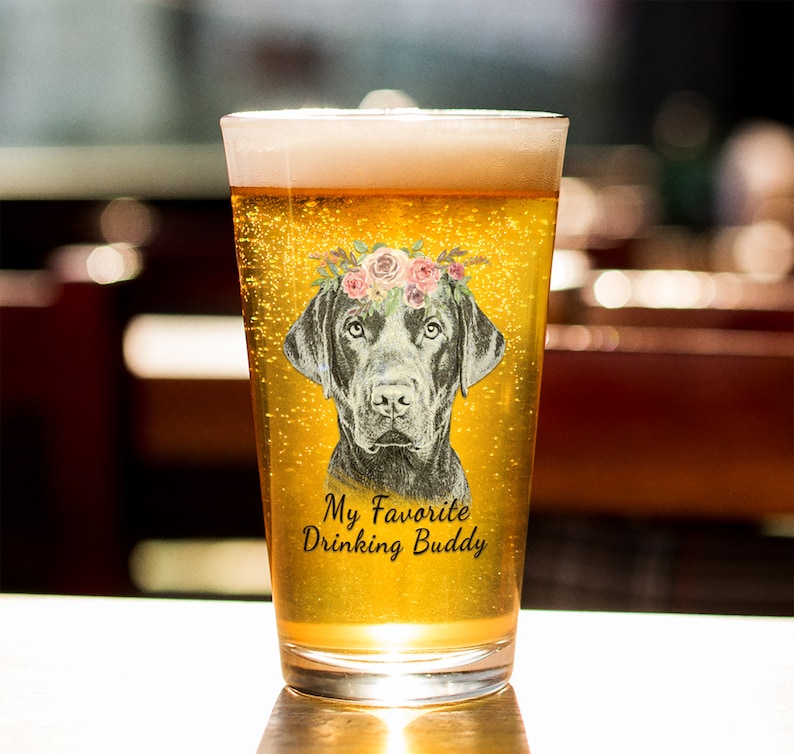 May include: A clear glass beer mug with a black Labrador Retriever wearing a floral crown. The mug has the text "My Favorite Drinking Buddy" printed on it.