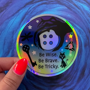 May include: A holographic sticker with a black cat, a key, a dragonfly, a button, and a triangle with a star inside. The sticker has the text "Be Wise. Be Brave. Be Tricky." and the text "Fortuna Pins" in the top right corner.