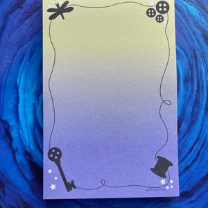 May include: A yellow and purple gradient card with a black border. The border is decorated with a dragonfly, buttons, a key, and a spool of thread. The card has the text "Fortuna Pins" in the bottom right corner.