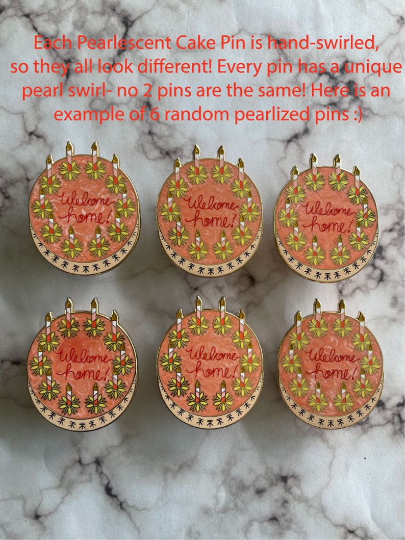 May include: Six round enamel pins shaped like cakes with a pearlescent pink swirled finish. Each pin features the text Welcome home! in red script, surrounded by yellow and white candles with gold metal outlines and a decorative border.