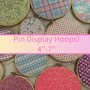 May include: A collection of pin display hoops with various fabric patterns and glitter. The hoops range from 4 to 7 inches in diameter. The text "Pin Display Hoops! 4"-7"" is displayed across the image.
