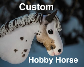 Könnte beinhalten: Ein weißes Steckenpferd mit braunen Flecken, einem dunkelbraunen Ohr und einer Mähne aus weißem und braunem Garn. Der Text 'Custom' steht oben und 'Hobby Horse' unten im Bild. Das Pferd hat ein realistisches Auge und eine hellbraune Schnauze.