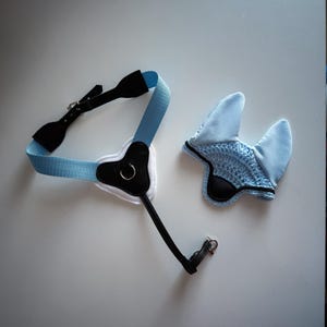 Peut inclure: Un ensemble de bride et de bonnet d'oreille pour cheval, bleu clair et noir. La bride présente une sangle bleu clair avec des accents de cuir noir et une boucle argentée. Le bonnet est bleu clair avec un centre crocheté.