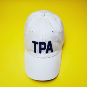 May include: A white baseball cap with a navy blue embroidered "TPA" on the front.