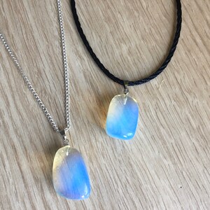 Op de afbeelding: Twee kettingen met iriserende opaal-stenen hangers. De ene ketting heeft een zilveren ketting en de andere een zwart koord.