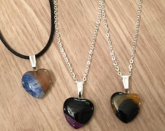 Könnte beinhalten: Drei herzförmige Halsketten mit unterschiedlich gefärbten Achat-Steinen. Die Halsketten liegen auf einer Holzoberfläche. Die Steine sind ein blauer und brauner Achat, ein schwarzer Achat mit violettem Rand und ein schwarzer und brauner Achat.