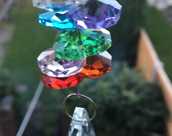 Op de afbeelding: Een kristallen zonenvanger met een traanvormig kristal aan de onderkant en een reeks gefacetteerde kristallen in regenboogkleuren erboven.