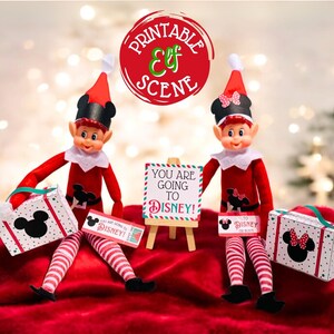 May include: Two elf dolls dressed in red and white striped outfits with black Mickey Mouse ears and a red bow. The elves are holding suitcases and a sign that says "You are going to Disney!"