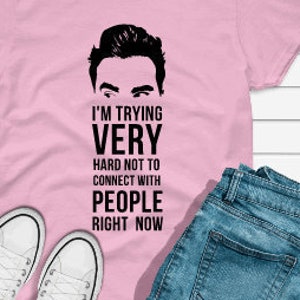 May include: Pink t-shirt with a black and white image of a man's face and the text "I'm trying very hard not to connect with people right now".