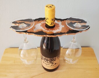 May include: A black and gold resin wine holder with two glass holders. The holder has a unique, organic shape and is perfect for serving wine and two glasses.