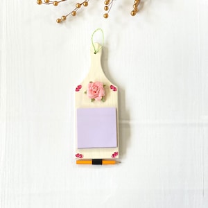 May include: White wooden memo board with a pink rose, a purple sticky note, and a yellow pencil. The board is decorated with pink and white hearts.