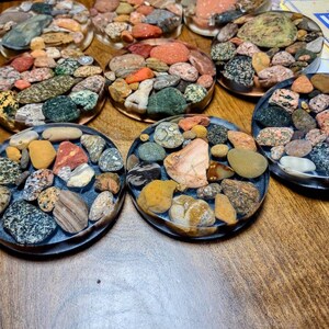 K&ouml;nnte beinhalten: Ein Set mit acht runden Untersetzern, die verschiedene farbige und gemusterte Steine ​​in klarem Harz eingebettet haben. Die Untersetzer haben einen Durchmesser von etwa 10 cm und eignen sich perfekt zum Schutz von Oberfl&auml;chen vor Hitze und Kratzern.