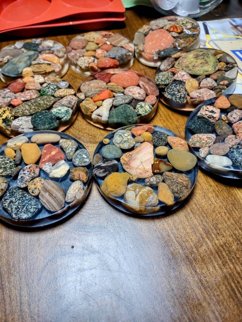 K&ouml;nnte beinhalten: Ein Set mit acht runden Untersetzern, die verschiedene farbige und gemusterte Steine ​​in klarem Harz eingebettet haben. Die Untersetzer haben einen Durchmesser von etwa 10 cm und eignen sich perfekt zum Schutz von Oberfl&auml;chen vor Hitze und Kratzern.