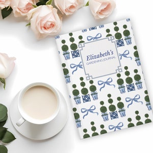 May include: A white gardening journal with a blue and green topiary pattern. The cover features the text "Elizabeth's Gardening Journal" in a black frame.