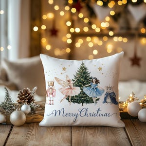 May include: White square pillow with a Christmas theme. The pillow features a watercolor illustration of a Christmas tree, a nutcracker, a fairy, a ballerina, and a mouse. The words "Merry Christmas" are written in a script font.