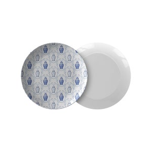 May include: Two white ceramic plates. One plate features a repeating blue and white pattern of decorative urns and floral elements. The other plate is plain white.