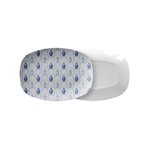 May include: Two white rectangular serving platters. One platter features a blue and white pattern of decorative vases and floral elements. The other platter is plain white. The platters are designed for serving food.
