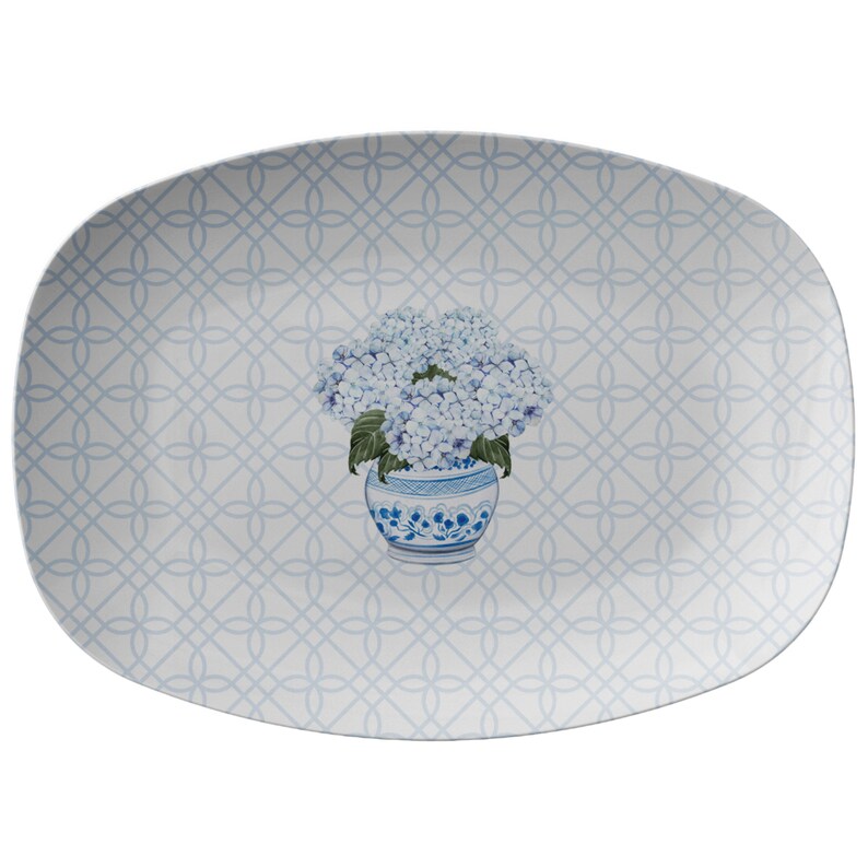 May include: A white oval serving platter with a blue and white geometric pattern. A blue and white vase with blue hydrangeas is in the center of the platter.