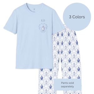 May include: Light blue pajama set featuring a short-sleeved top with a crest design and the initials "KB". The matching pajama pants have a white background with a blue vase pattern. A light blue circle indicates "3 Colors". The text "Pants sold separately" is also visible.