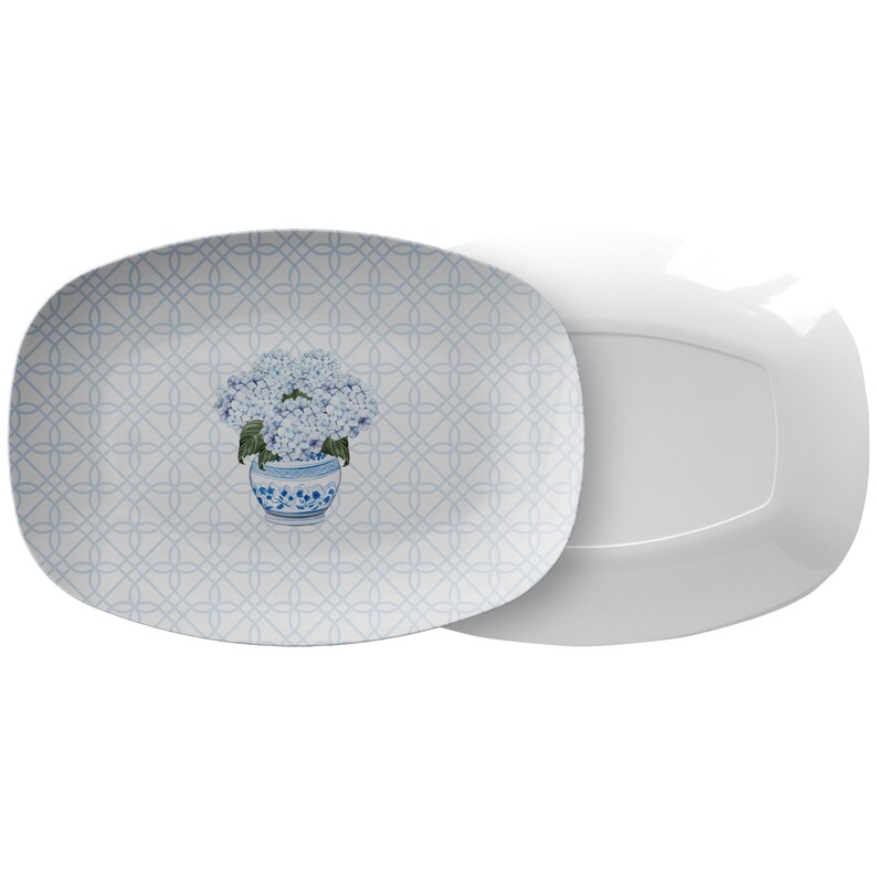 May include: A white oval serving platter with a blue and white floral pattern. The pattern features a bouquet of blue hydrangeas in a blue and white vase. The platter has a delicate lattice design.