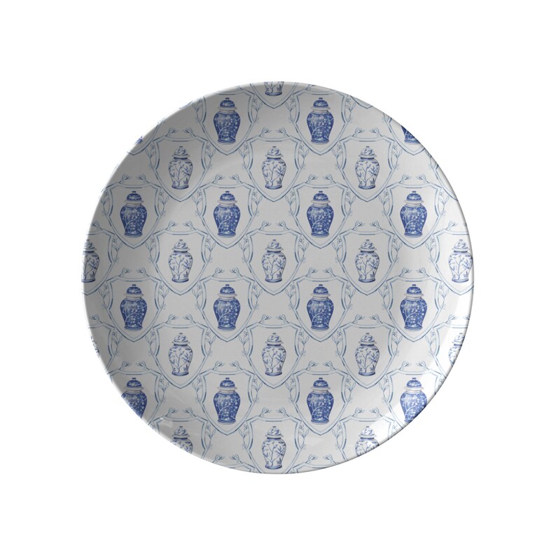 May include: White ceramic plate with a repeating blue and white pattern. The design features blue Chinese ginger jars within a shield-like frame. The plate has a glossy finish and a circular shape, suitable for serving food.