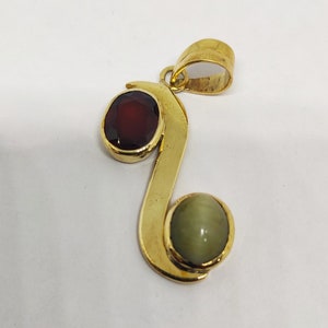 May include: Gold pendant featuring a red and green gemstone. The pendant is shaped like a stylised letter 'S'.