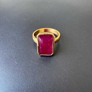 May include: A gold ring with a large, rectangular, deep red ruby gemstone.