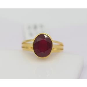 May include: A gold ring featuring a large, oval-shaped ruby gemstone. The ring has a simple, elegant design with a thin band and a slightly raised setting for the ruby.